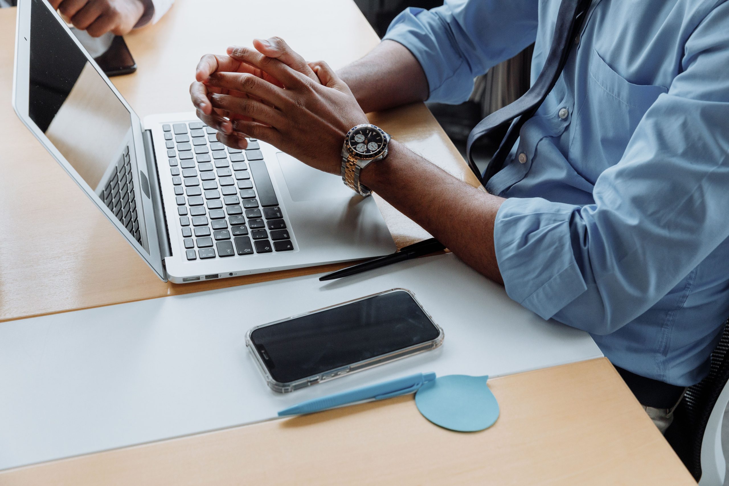 Close-up of a professional in an office with a laptop, smartphone, and wristwatch, exuding productivity.